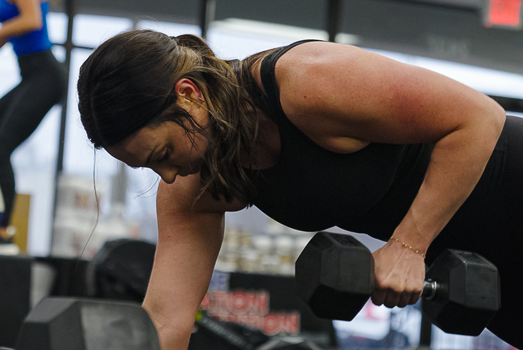 Woman performing a dumbbell row exercise during a strength training workout at Freedom Fitness O’Fallon.